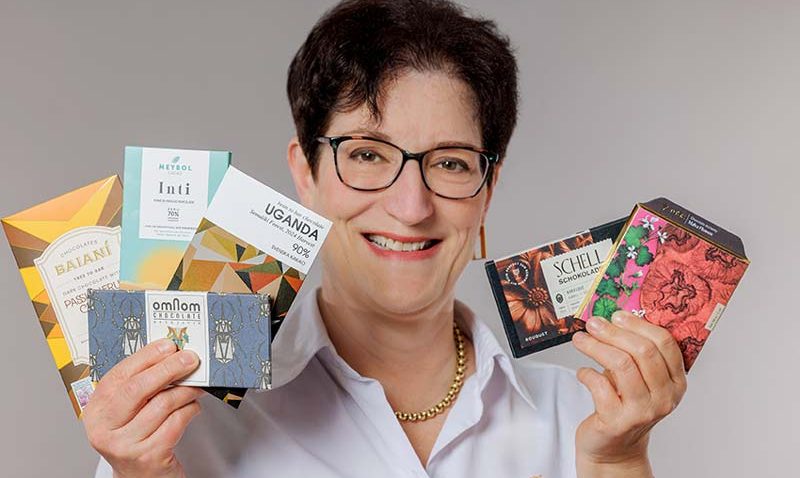 Frau mit Brille hält mehrere bunte Schokoladen in einem Fächer in den Händen.